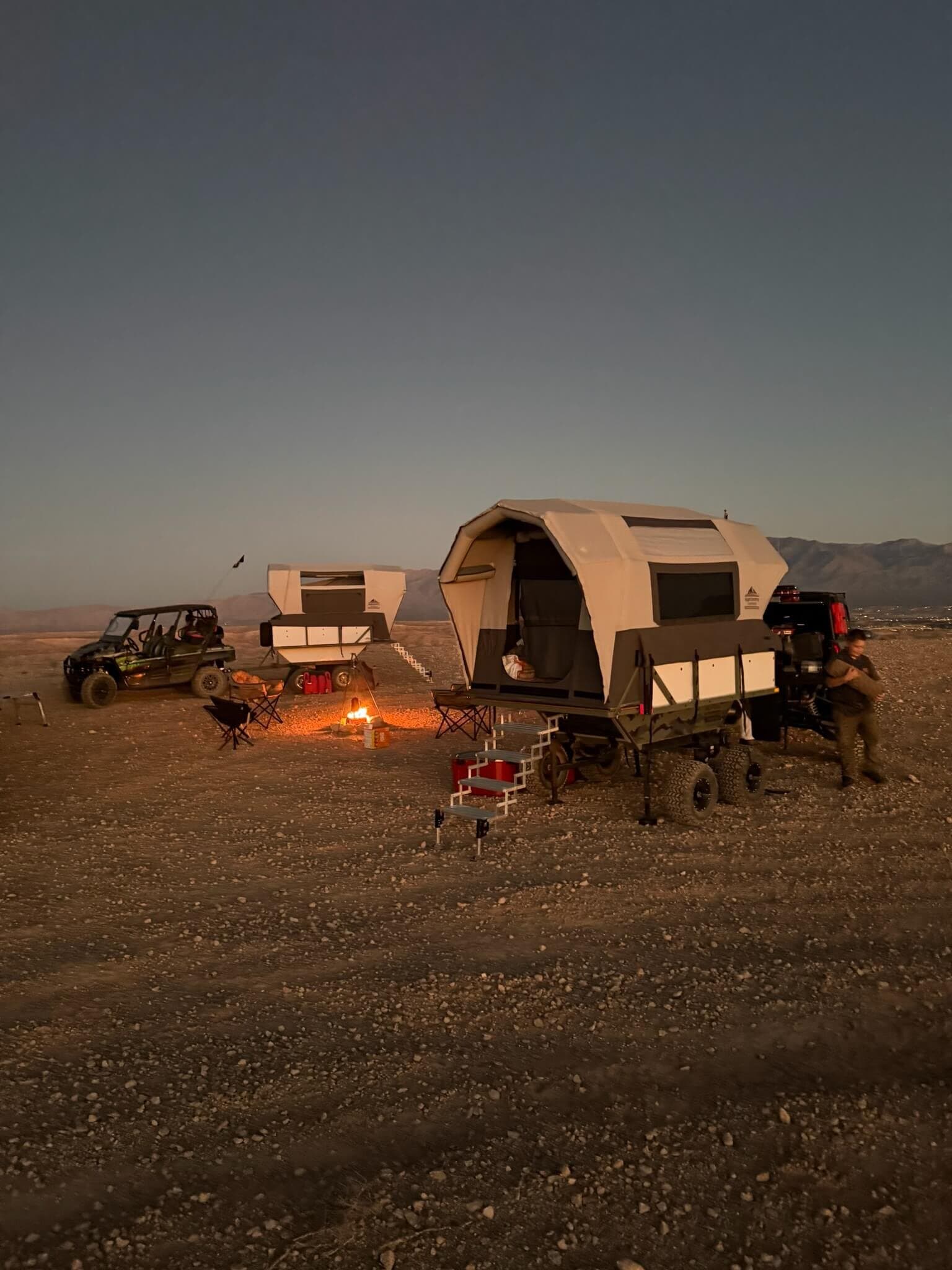 Two Conestoga Campers set up around a fire at dusk in the Nevada desert
